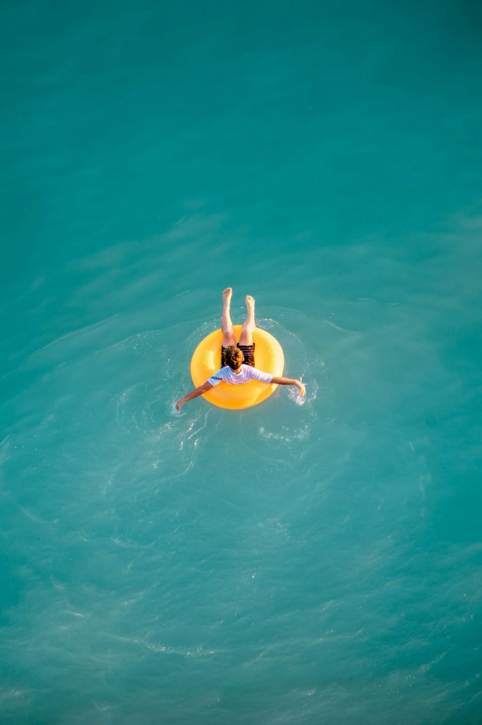A person floating on a yellow inner tube in clear turquoise water, with arms outstretched.